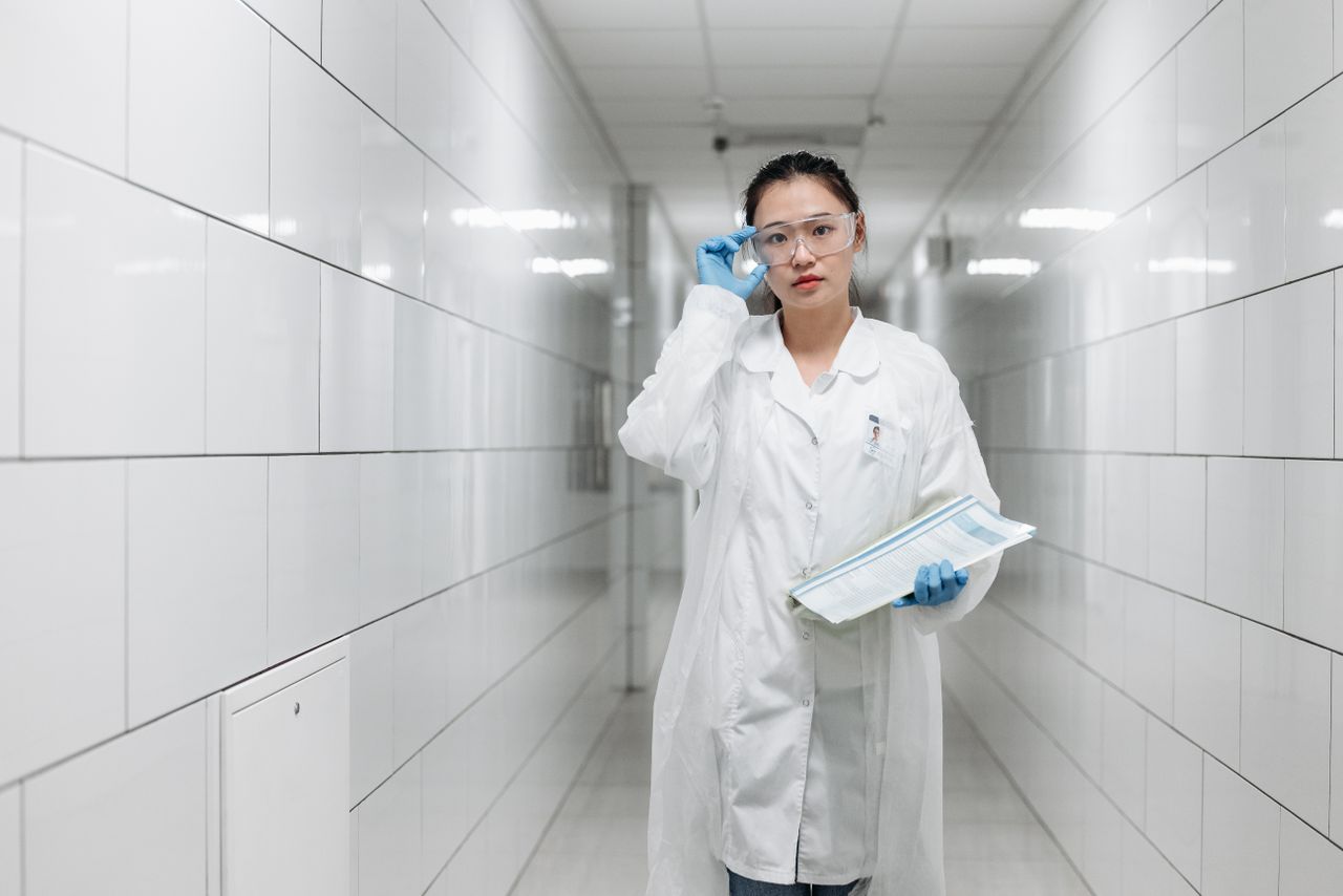 services-03 Asian female scientist walking in a laboratory corridor with protective goggles and a lab coat.