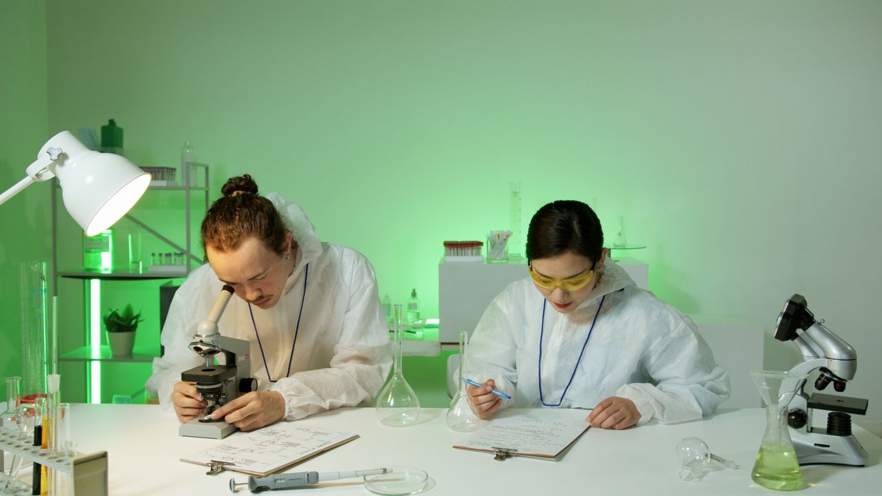 services-02 Two scientists in protective gear working with microscopes in a lab environment.