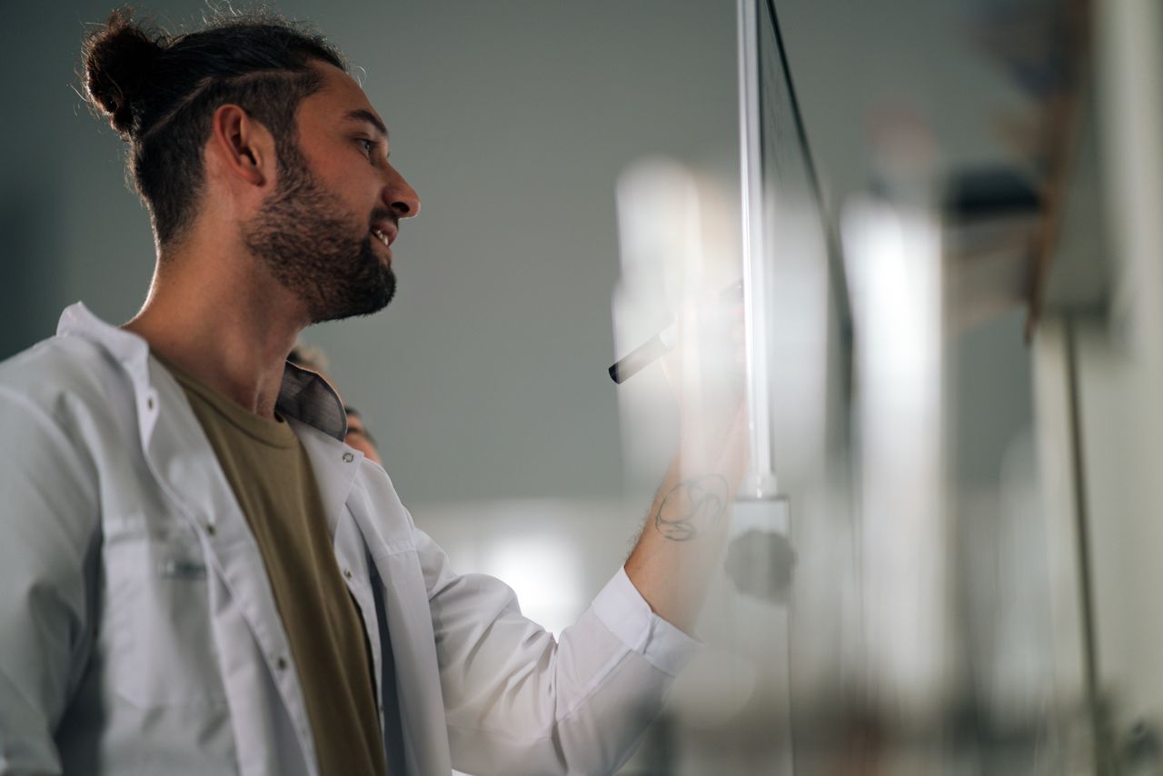 services-01 A young scientist writing on a whiteboard in a lab setting, focused on research ideas.